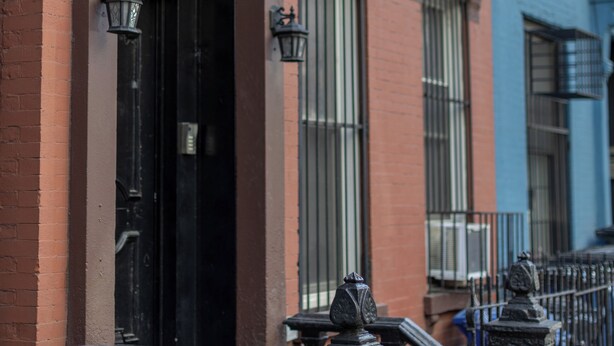 A row of red brick townhouses with black doors and windows, a black metal fence, and a small trash bin in front. - Manhattan Bridge-Brooklyn-UN (Brooklyn)