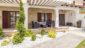 A two-story building with a covered patio area featuring outdoor furniture and a stone wall.