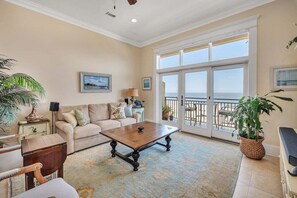 A spacious living room with a large window, a sofa, a coffee table, and a potted plant. - Sea Point Condo #307 (Saint Simons Island)