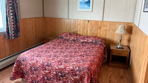 A bedroom with a wooden headboard, a patterned bedspread, a nightstand with a lamp, and a framed picture on the wall.