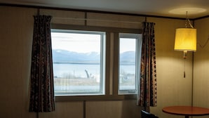 A hotel room with a large bed, two windows with curtains, a small table, and a lamp.