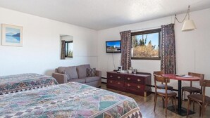 A room with two beds, a sofa, a TV, a table with chairs, and a dresser.