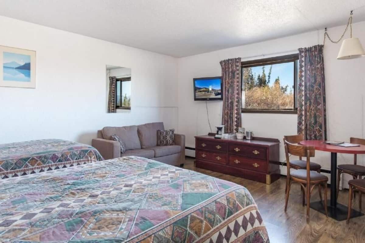 A room with two beds, a sofa, a TV, a table with chairs, and a dresser.