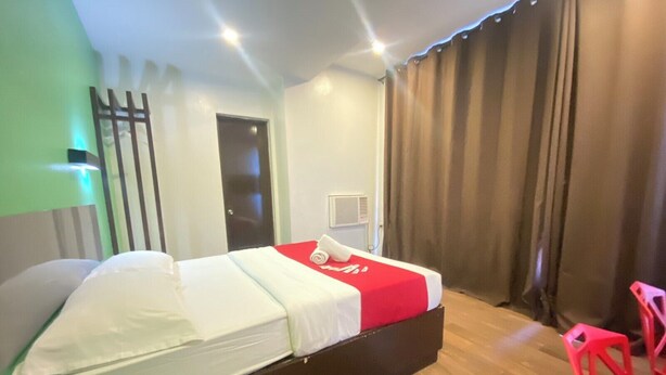 Une chambre d’hôtel avec un lit, une chaise rouge, une porte et une fenêtre avec des rideaux.