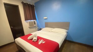 Une chambre d’hôtel avec un lit, une couvre-lit rouge et blanche, un oreiller blanc et un rideau marron.