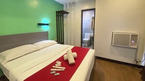 Une chambre d’hôtel avec un lit, un mur vert, un plafond blanc et une salle de bain visible à travers une porte ouverte.