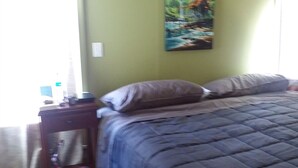 A bedroom with a bed, a nightstand, a painting on the wall, and a window.