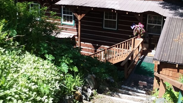 A rustic log cabin with a steep staircase leading to a porch.