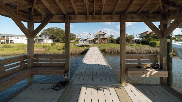 A wooden deck with benches, a pathway leading to a grassy area, and houses in the background. - New! Intracoastal Cottage with Dock! (Surf City)