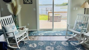A room with a view of a dock and water, featuring rocking chairs, a clock, and a door leading outside. - New! Intracoastal Cottage with Dock! (Surf City)