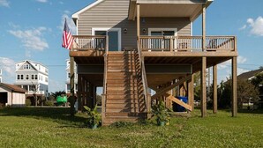 A two-story house with a wooden deck and a balcony. - New! Intracoastal Cottage with Dock! (Surf City)