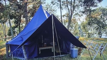 Una carpa azul con entrada elevada, rodeada de árboles y una valla de metal.