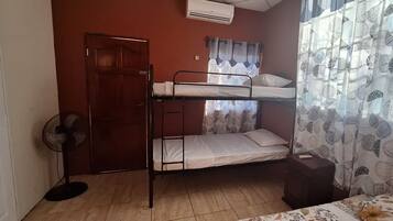 Un dormitorio con literas, un ventilador de pie, un armario y una ventana con cortinas estampadas.