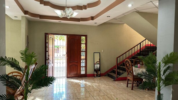Un vestíbulo amplio con piso de baldosas, una escalera de madera y una gran puerta que da al exterior.