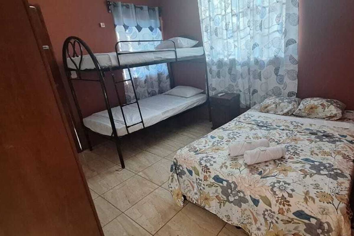 A dormitory room with bunk beds, a single bed, and a window with curtains.