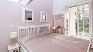 Un dormitorio con cama, mesita de noche, lámpara, ventana y puerta que da a un espacio exterior.