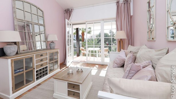 Una habitación con un ventanal grande, un sofá blanco, una mesa de centro de madera y un aparador con puertas de cristal.