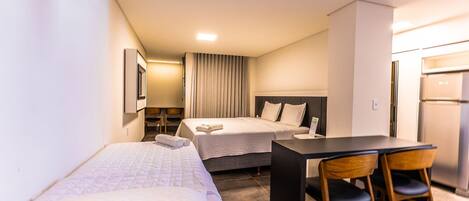 A hotel room with two beds, a desk, chairs, a refrigerator, and a ceiling-mounted air conditioner.