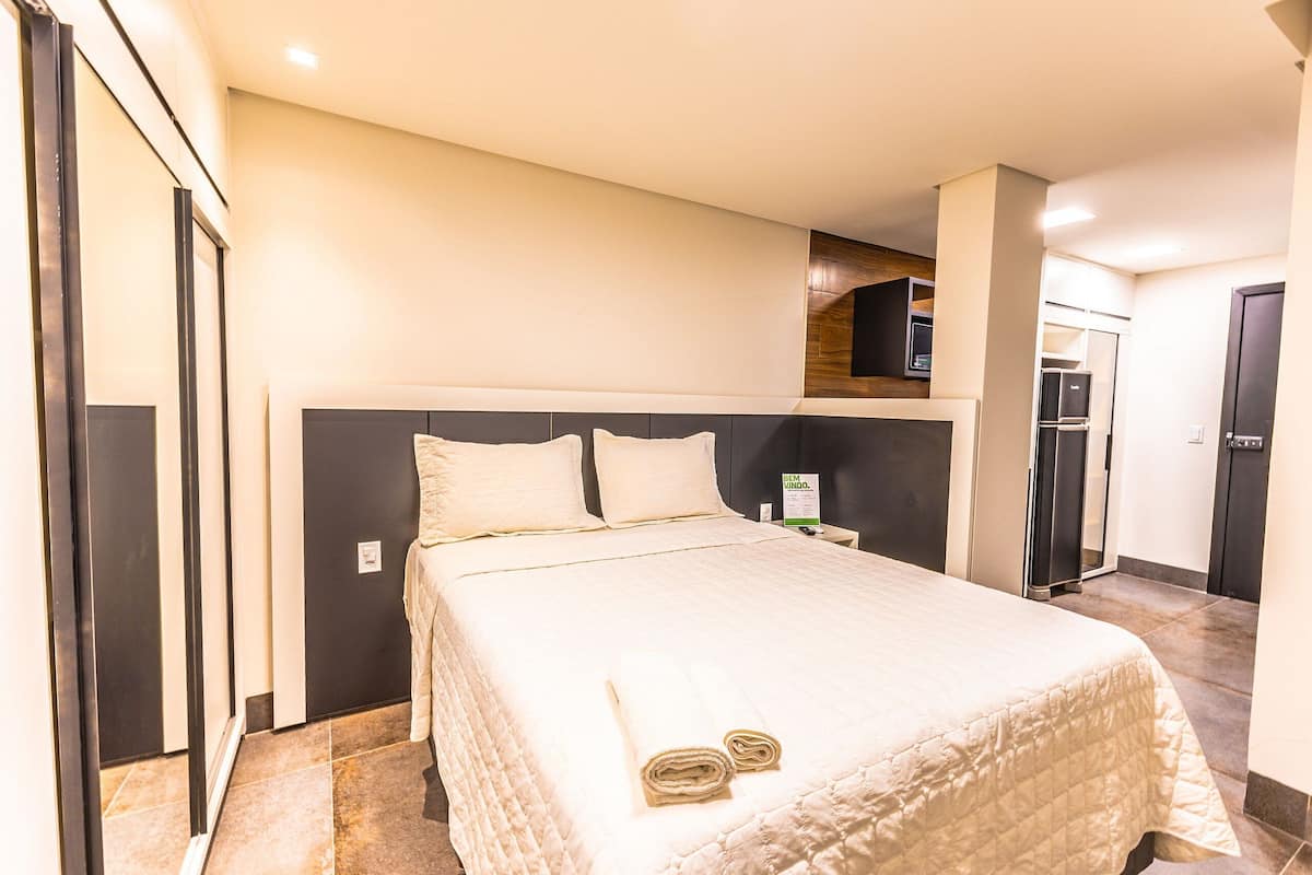Une chambre d’hôtel avec un grand lit, une armoire, un miroir et une petite table.