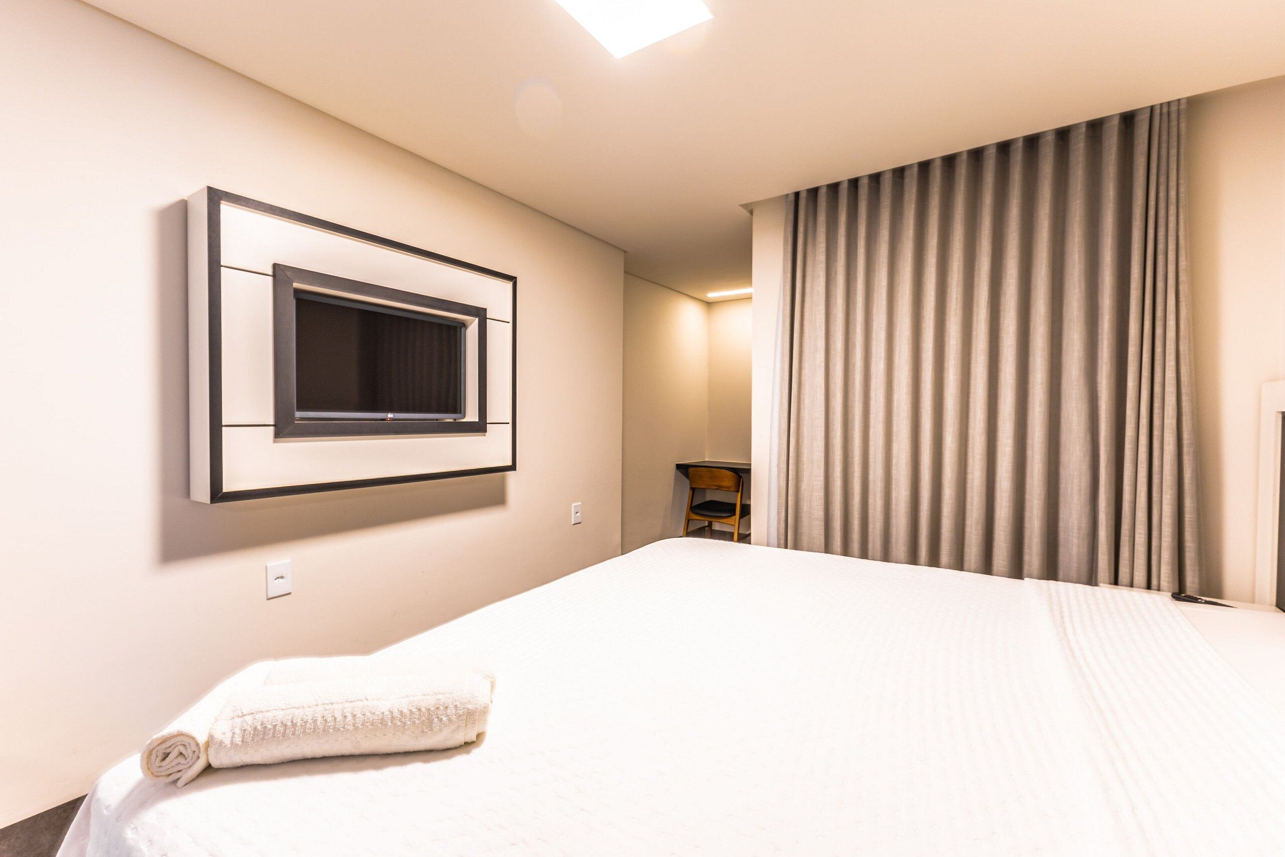Ein Hotelzimmer mit einem Bett, einem an der Wand befestigten Fernseher, einem Sessel und einem Vorhang.