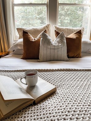 A neatly made bed with a knitted rug, a cup of tea, and an open book on a wooden floor. - Woolrich Cottage at Woolrich Estate (Olinda)
