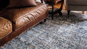 A living room with a brown leather sofa, a white armchair, a wooden cabinet, and a patterned rug. - Woolrich Cottage at Woolrich Estate (Olinda)