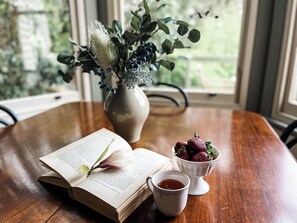 An open book on a wooden table with a vase of flowers and a bowl of strawberries. - Woolrich Cottage at Woolrich Estate (Olinda)