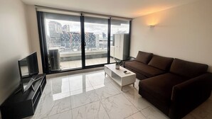 A modern living room with a large window, a brown sofa, a white coffee table, and a TV on a stand.