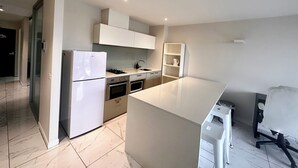 A modern kitchen with white cabinetry, a built-in oven, and a stainless steel refrigerator.