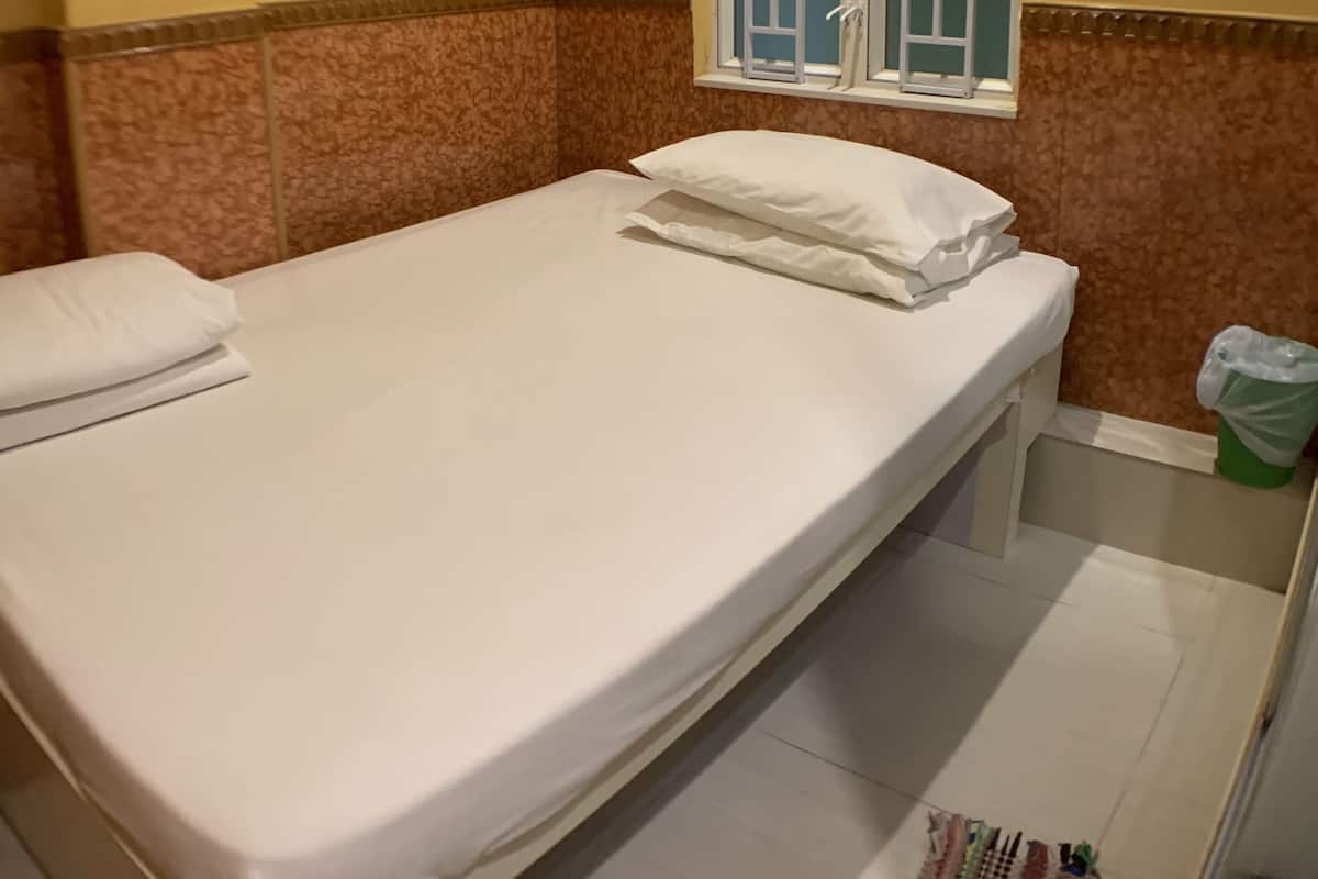 Ein Hotelzimmer mit einem Einzelbett, einem Fenster mit Ausblick, einer Wandklimaanlage und einer kleinen Mülleimer.