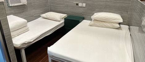 A hotel room with two single beds, a small table, and a wall-mounted air conditioner.
