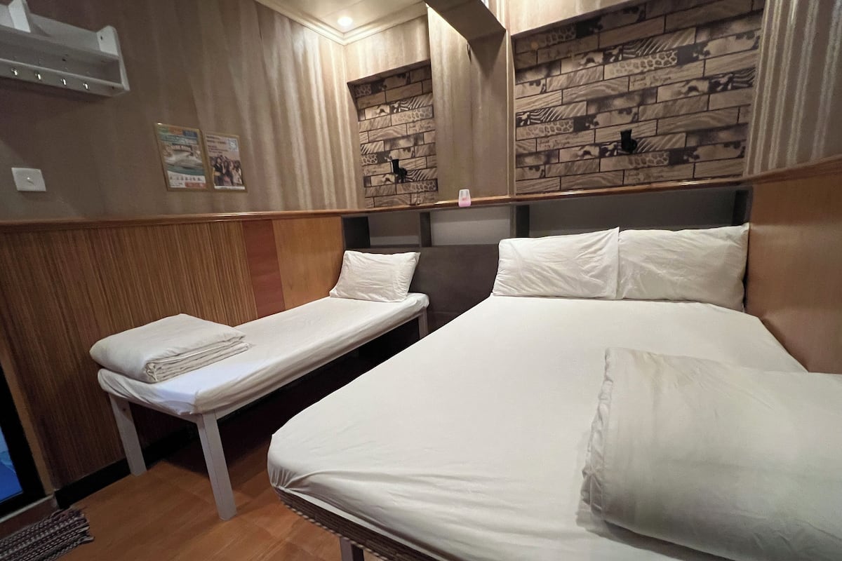 Ein Hotelzimmer mit zwei Betten, Holzboden, einer Wand mit Ziegelmuster und einem kleinen Tisch mit einem Handtuch.