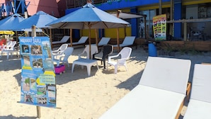 A beachside area with lounge chairs and umbrellas, a signboard with information, and a building with a balcony. - Miramar Baru (Cartagena)