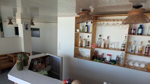 A bar area with a counter, shelves with bottles and glasses, and a wooden bench. - Miramar Baru (Cartagena)