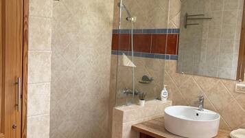 Un baño con puerta de madera, cabina de ducha de vidrio, lavabo con espejo y toallero.