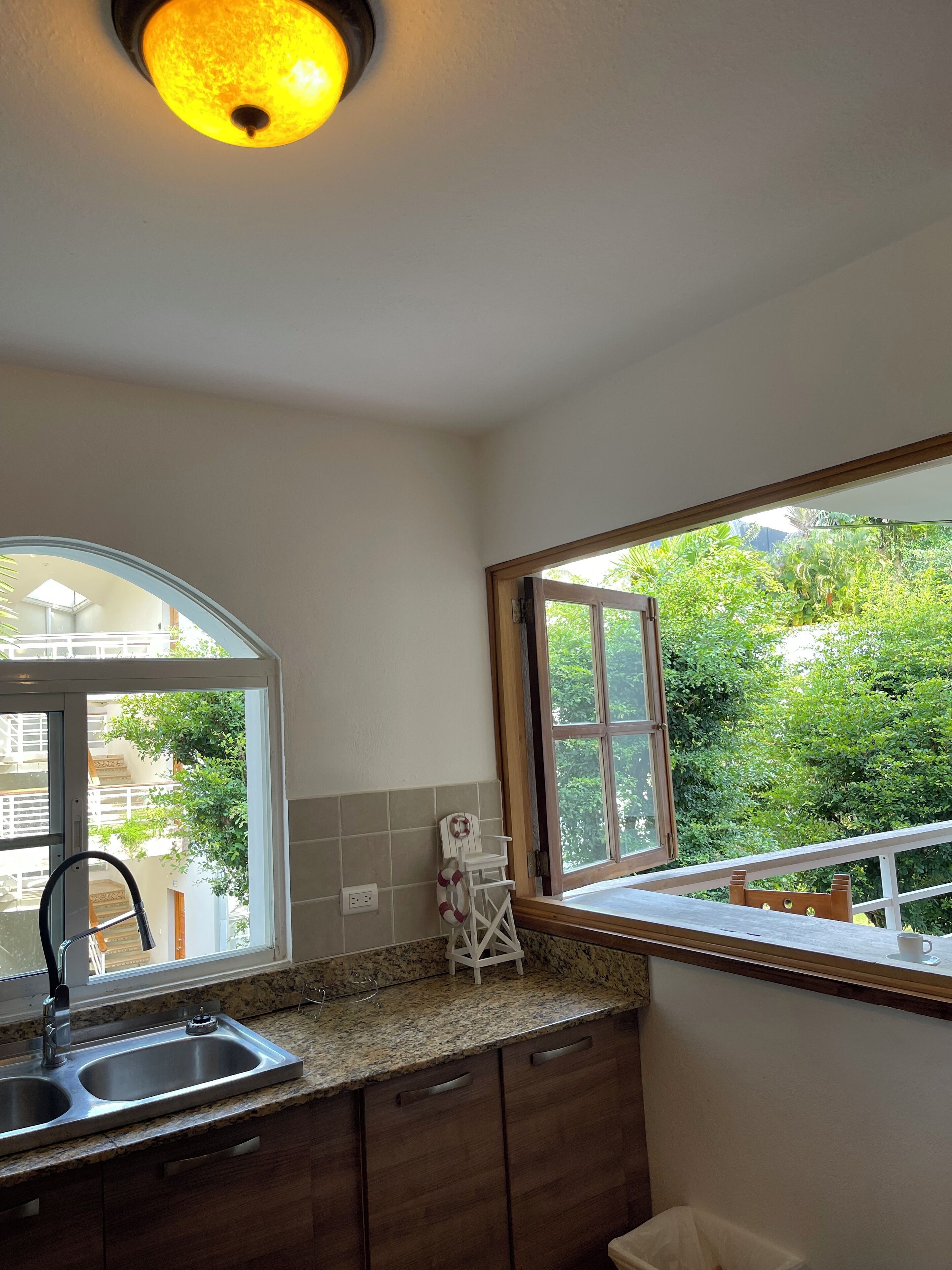 A kitchen with a granite countertop, stainless steel sink, wooden cabinets, and a window overlooking greenery.