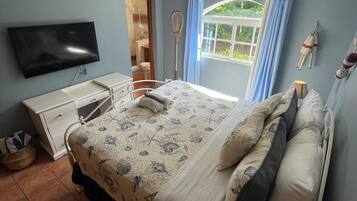 Une chambre à coucher comprenant un lit, un téléviseur, un ventilateur de plafond, une fenêtre avec des rideaux et une lampe de chevet.
