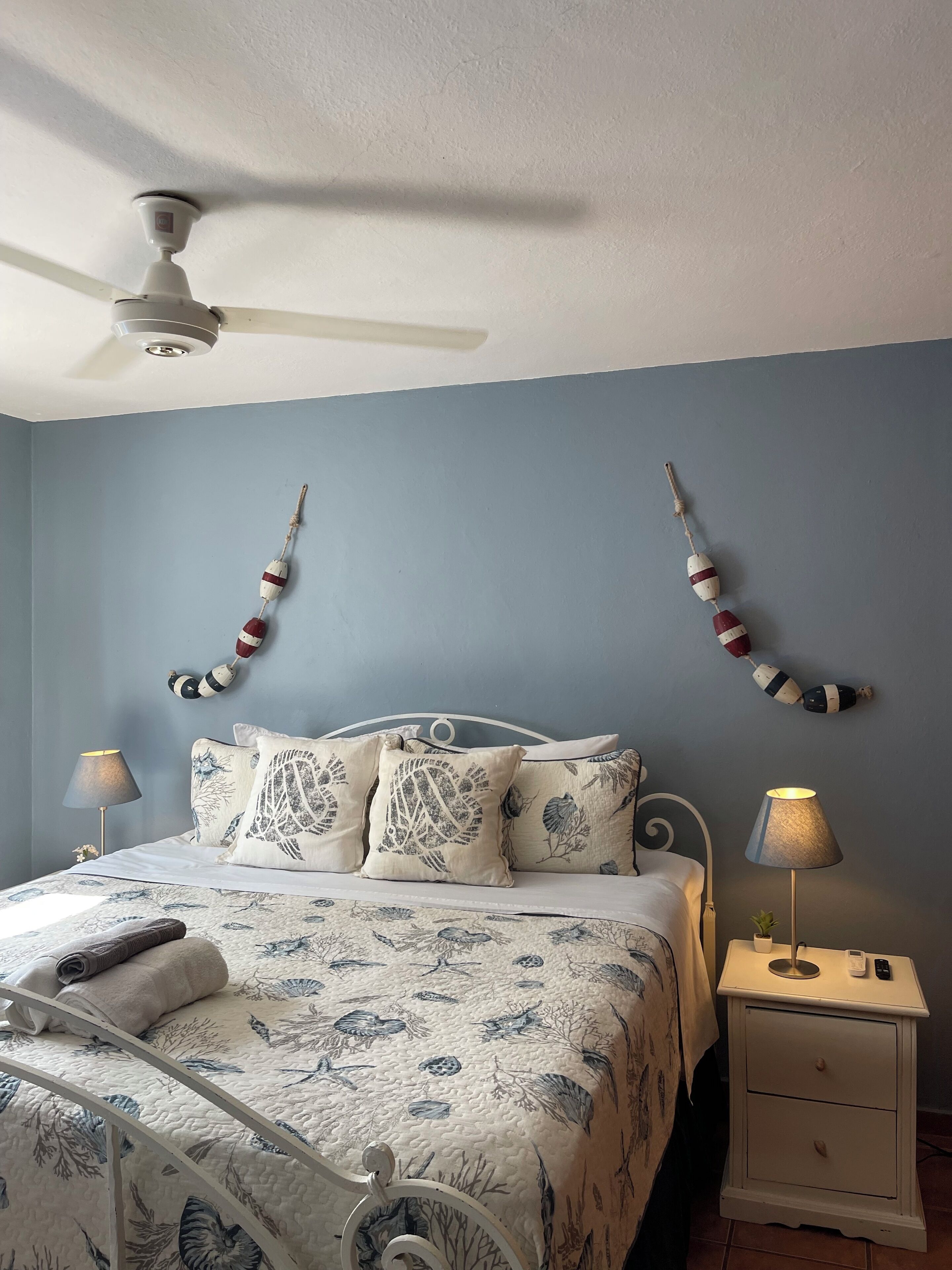 Een slaapkamer met een bed, twee nachtkastjes, een plafondventilator en wanddecoraties.