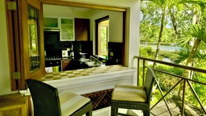 A balcony with a checkered table and chairs, a kitchen area with a stove and sink, and a view of greenery and water. - BonitaVillageLasTerrenas 4Beds8Pax (Las Terrenas)