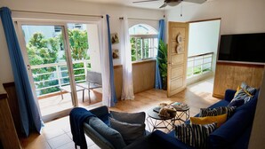 A living room with a sofa, a coffee table, and a TV. There is a balcony with a railing and a door leading outside. - BonitaVillageLasTerrenas 4Beds8Pax (Las Terrenas)