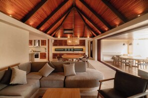 A modern interior with a sloped ceiling, a sectional sofa, a dining area, and a kitchen in the background.