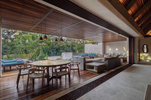 An open-plan living area with a wooden deck, outdoor seating, and a view of greenery.