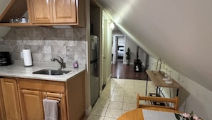 A kitchen with wooden cabinets, a stainless steel sink, and a refrigerator. There is a dining area with a wooden table and chairs, and a small potted plant on the table.