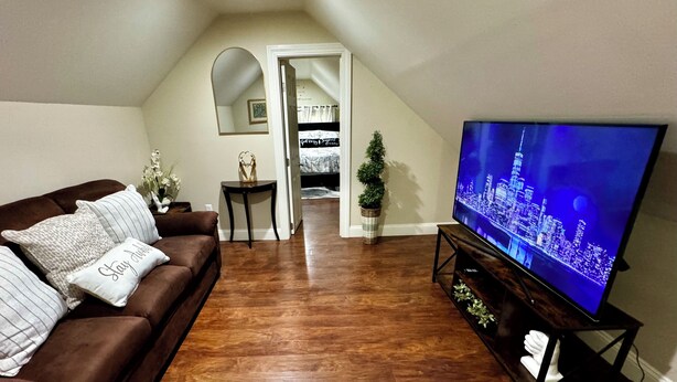A living room with a brown leather sofa, a flat-screen TV on a stand, a small table, and a potted plant.