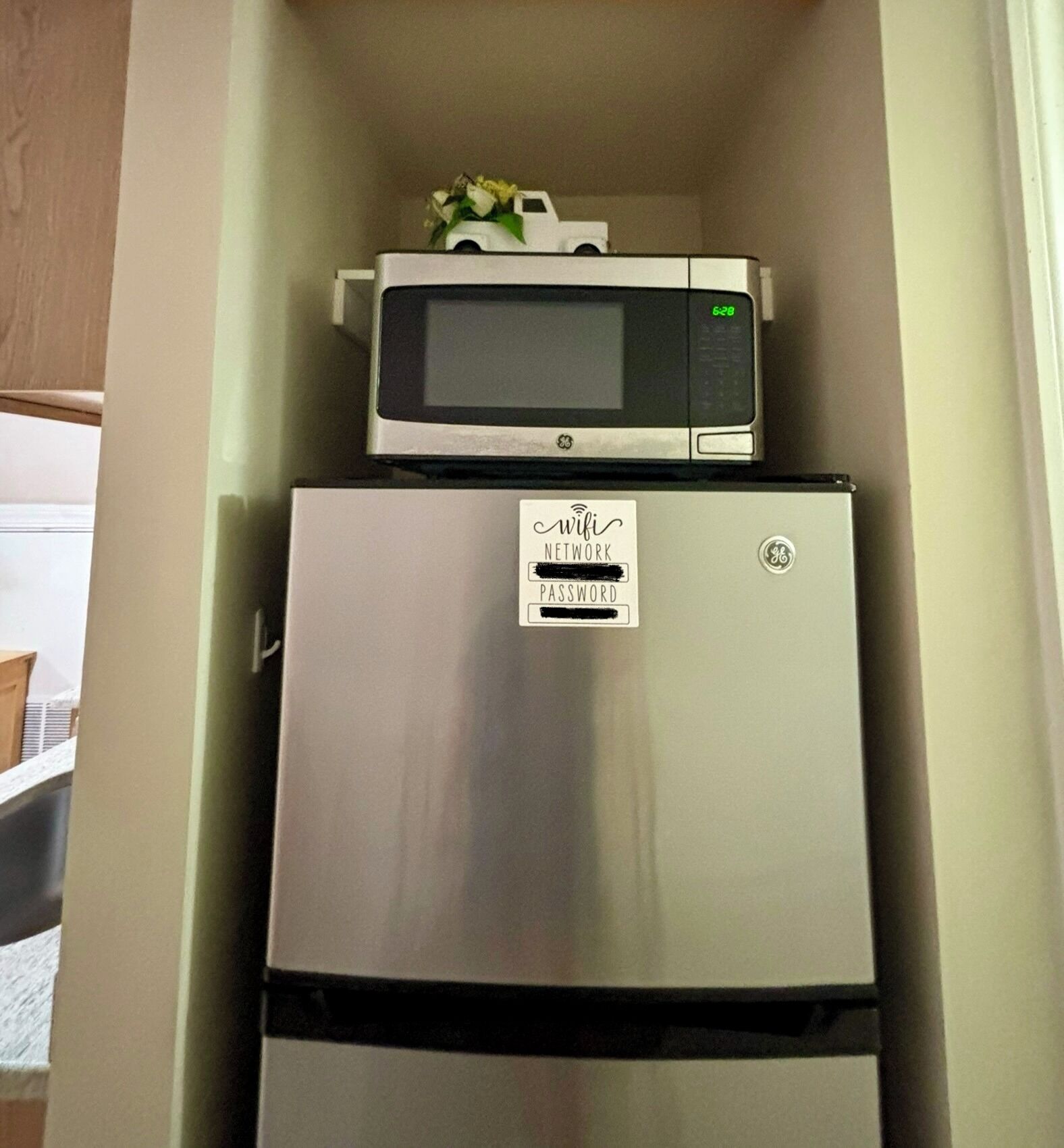 A compact kitchen with a stainless steel refrigerator and a microwave on top.