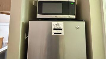 A compact kitchen with a stainless steel refrigerator and a microwave on top.