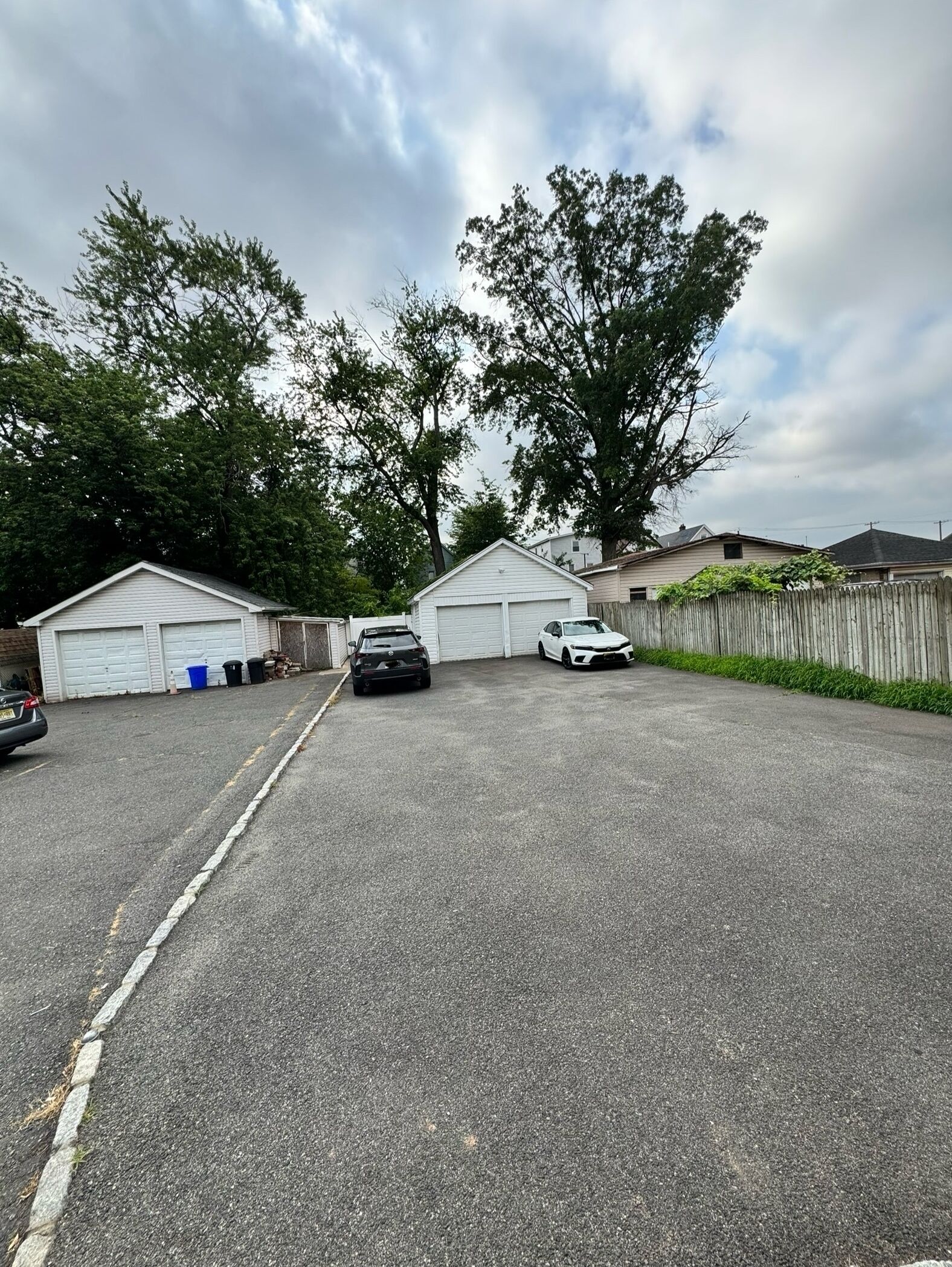 Eine Garage mit zwei Autos, umgeben von Bäumen und einem Holzzaun.