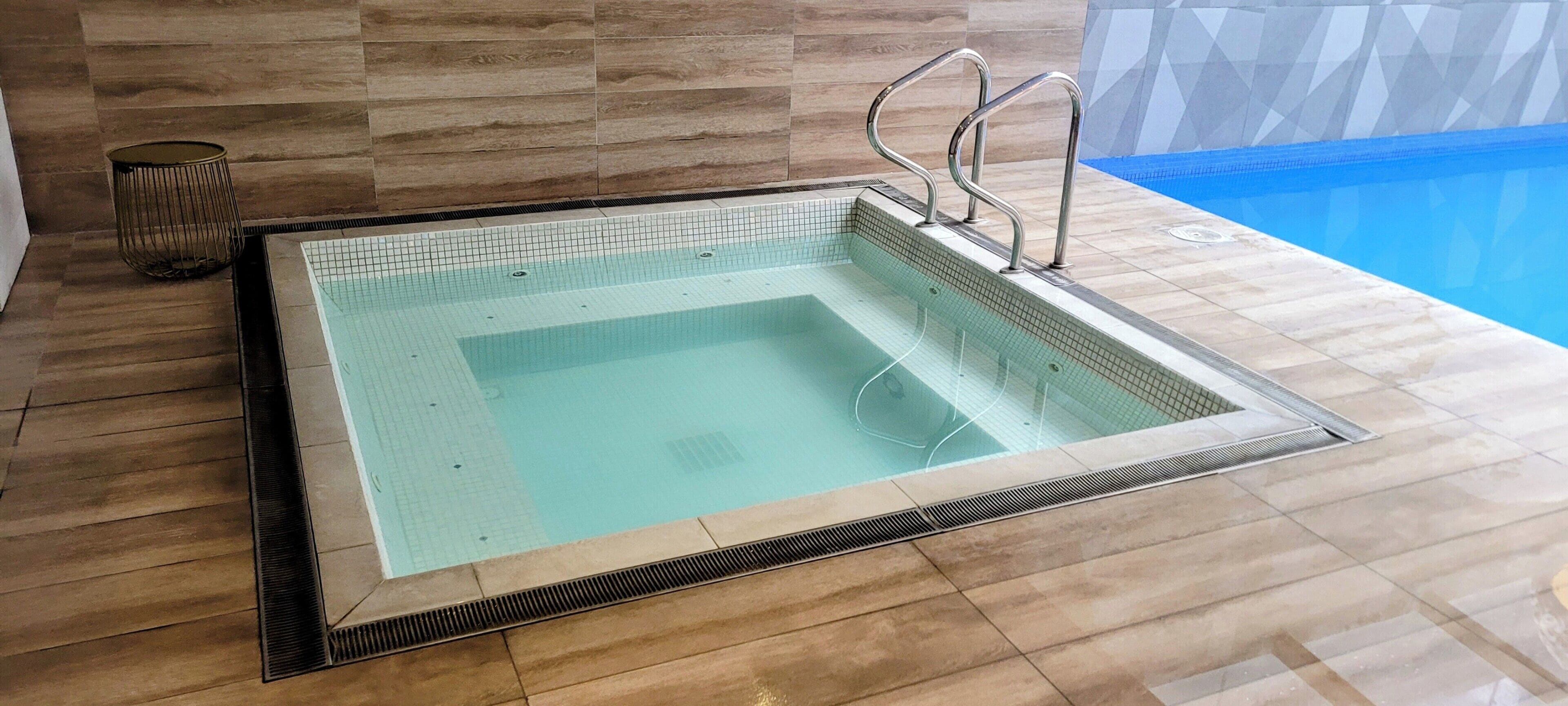 Una piscina interior rectangular con borde de azulejos y barandillas de metal.