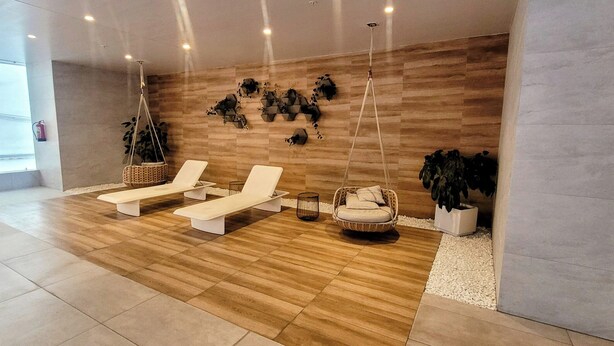Uma área de spa moderna com piso de madeira, espreguiçadeiras brancas, uma cadeira suspensa e arte decorativa nas paredes.