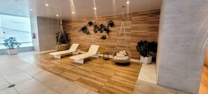 Moderni spa-alue, jossa on puulattia, valkoiset lepotuolit, riipputuoli ja koristeelliset seinätaideteokset.